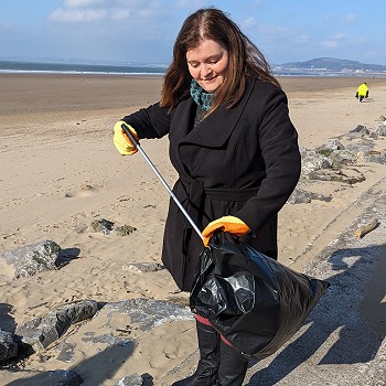 Dynes yn casglu sbwriel ar draeth ar ddiwrnod cynnes