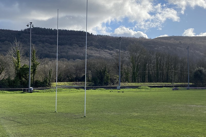 cae rygbi gyda phost a mynyddoedd yn y cefndir