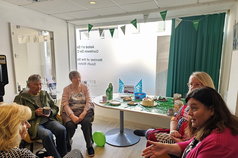 Mae Sioned Williams MS yn mynychu bore coffi er budd Cymorth Canser Macmillan yn fy swyddfa yng Nghastell-nedd wedi'i hamgylchynu gan grŵp o bobl.