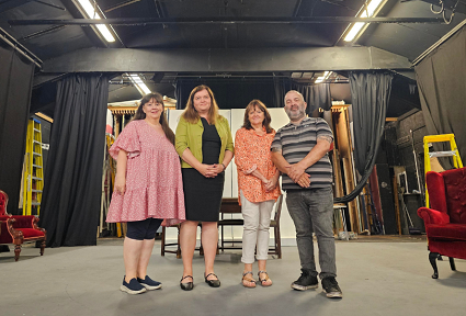 Sioned Williams standing on a theatre stage with three other people