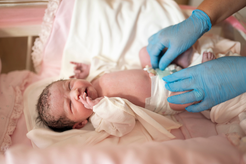 new born baby with someone in blue plastic gloves about to open its nappy