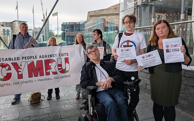 Sioned ac ymgyrchwyr y tu allan i'r Senedd yn dal baneri mae un mewn cadair olwyn