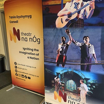 Two Theatr na nÔg promotional banners in a theatre foyer, featuring photographs from stage productions and the slogan “Igniting the Imagination of a Nation”.